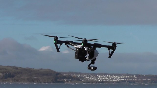 Small camera drone rotates to face the viewer and then flies out of frame.