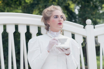Tea drinking victorian woman sitting on garden seat.