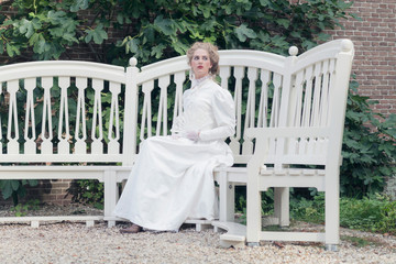 Victorian woman with fan sitting on garden seat.