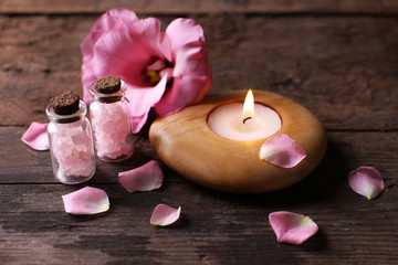 Tenderness composition of alight candle with flower petals on wooden background