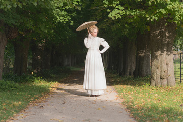 Chique victorian womanwith umbrella walking on path in garden.