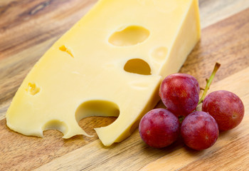 Maasdam cheese with grapes on the wooden board.
