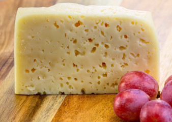 Swiss cheese with grapes on the wooden background.