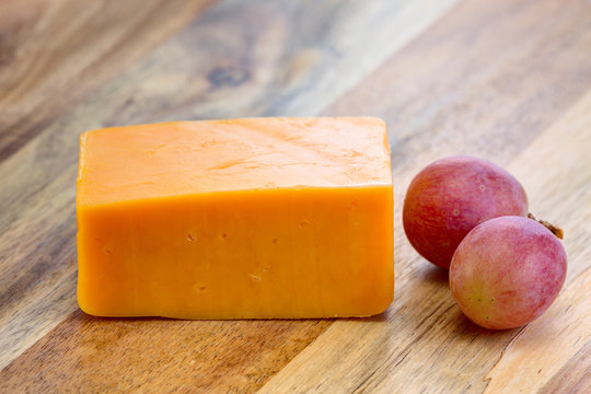 Red cheddar cheese with grapes on the wooden board.