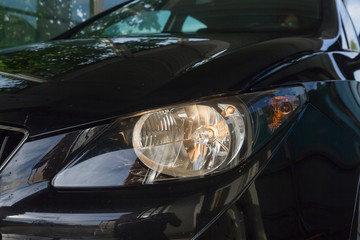 Detalle de Faro enecendido de coche metalizado negro, con reflejos en la chapa