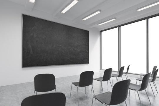 A classroom or presentation room in a modern university or fancy office. Black chairs, a black chalkboard on the wall and panoramic windows with white copy space. 3D rendering.