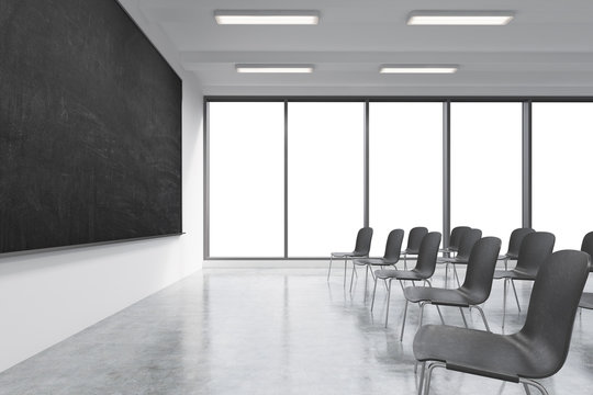 A classroom or presentation room in a modern university or fancy office. Black chairs, a black chalkboard on the wall and panoramic windows with white copy space. 3D rendering.