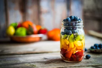 Raamstickers Colorful fruit salad in a jar on rustic wooden background © ehaurylik