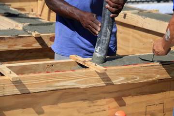 Pouring wet cement to create a tie beam for a concrete block wall is a team effort, and action...
