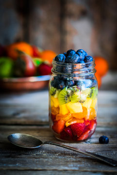 Colorful fruit salad in a jar on rustic wooden background