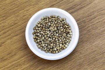 Dry coriander in white bowl on wooden table