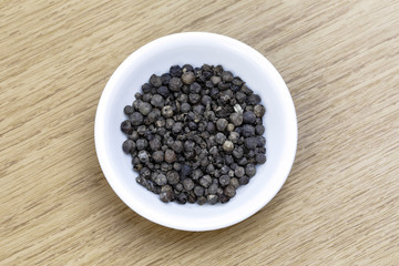 Dry black pepper in white bowl on wooden table