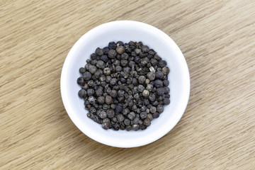 Fototapeta na wymiar Dry black pepper in white bowl on wooden table