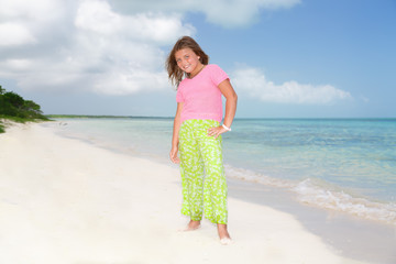 portrait of a little beautiful pretty fashionable girl standing on Cuban beach against turquoise ocean and blue sky background