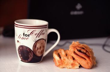  Cup of coffee with croissant and a laptop on background