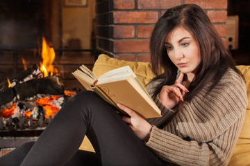 Woman reading a book by fireplace