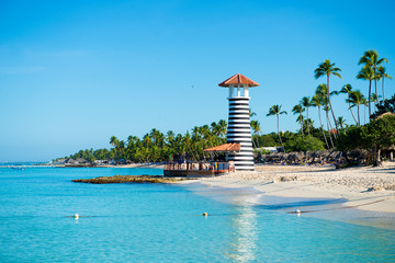 Transparent sea water and clear sky. Lighthouse on a sandy tropical island with palm trees.