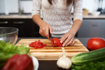 girl chops tomato on salad in the kitchen