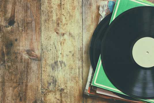 selective focus of records stack with record on top over wooden table. vintage filtered
