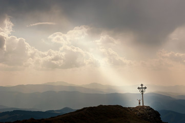 Man stands near the cross on top of mountain