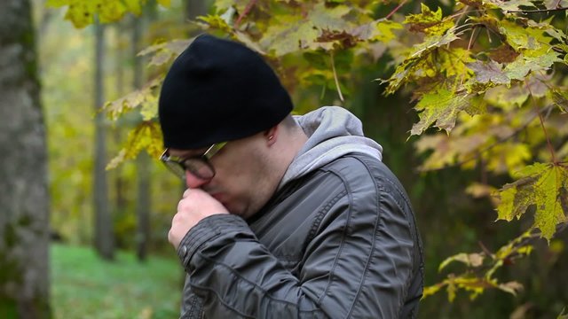 Sick ill man with fever and cough in autumn in the park 
