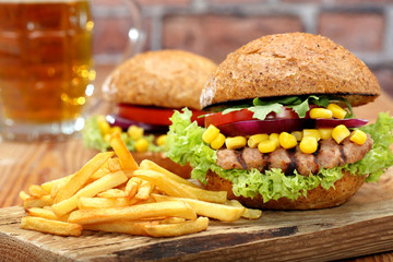 Grilled hamburger with fries, tomato, onion and corn on wooden b