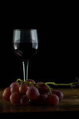 Bottiglia e bicchiere di vino rosso con uva rossa su tavolo antico sfondo nero e tavolo antico