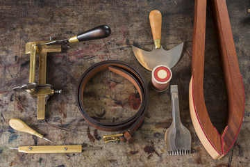 Fototapeta na wymiar Leather goods craftsman's tools and a ready belt on a dirty work bench