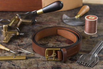Leather goods craftsman's tools and a ready belt on a dirty work bench