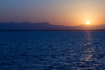 Sonnenuntergang vom Meer aus, im Hintergrund sind Berge zu sehen