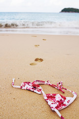 Fototapeta na wymiar Bikini top lying on beach with footprints into surf