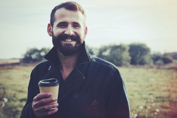 Bearded man with paper cup of morning coffee walking in park