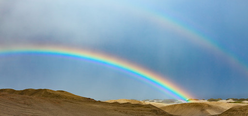 Desert landscape with a colorful rainbow and heavy rain clouds,