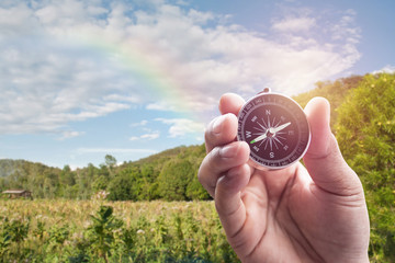 Compass in hand on blur of mountain view with rainbow for backgr