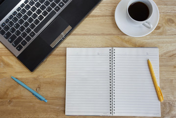Blank notepad over laptop and coffee cup on office wooden table