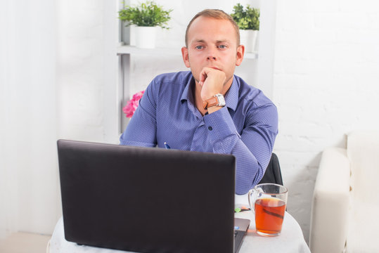 Businessman working in office, sitting at table with a laptop, looking camera.