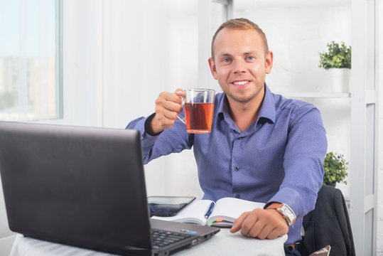 Businessman working in office, sitting at a table holding cup and looking straight.