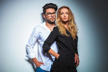 couple pose in studio with hands in pockets while looking at the