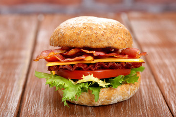 Bacon burger with tomato and cheese on wooden table