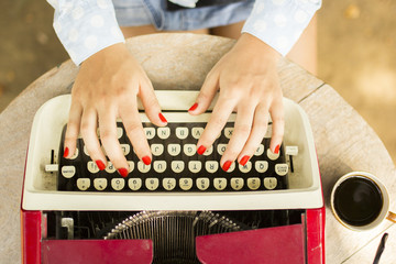 Girl typing on the old typewriter with a cup of coffee outdoors