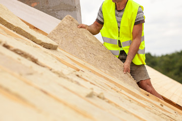 Roofer builder worker installing roof insulation material on new house under construction