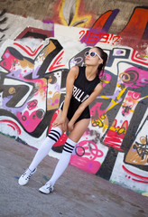 Beautiful woman with black sunglasses and black sport clothing sexy dancing in front of graffiti wall