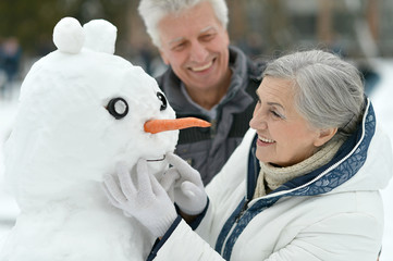 Happy senior couple with snowman