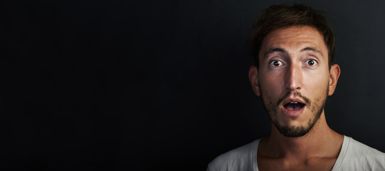 Portrait of cute young man wearing white tshirt and looks surprised. Wide