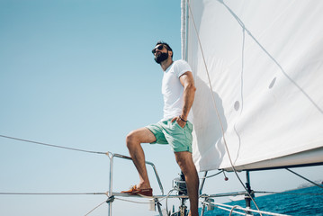 Low angle view of young bearded man standing on the yacht