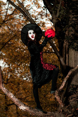 Naklejka premium Teenage girl dressed in witch costume sitting on the tree