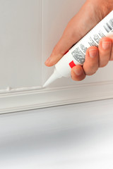 Hands caulking bath tube with white silicone glue