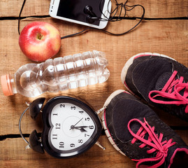 Sport equipment. Sneakers, water, apple, alarm clock, smartphone and earphones on wooden background. Clothes for running. Morning running concept