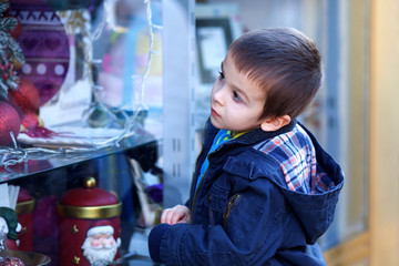 Sweet little boy, looking through a window in shop, decorated fo