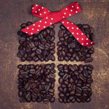 A red ribbon bow on top of a dark roasted coffee beans present o